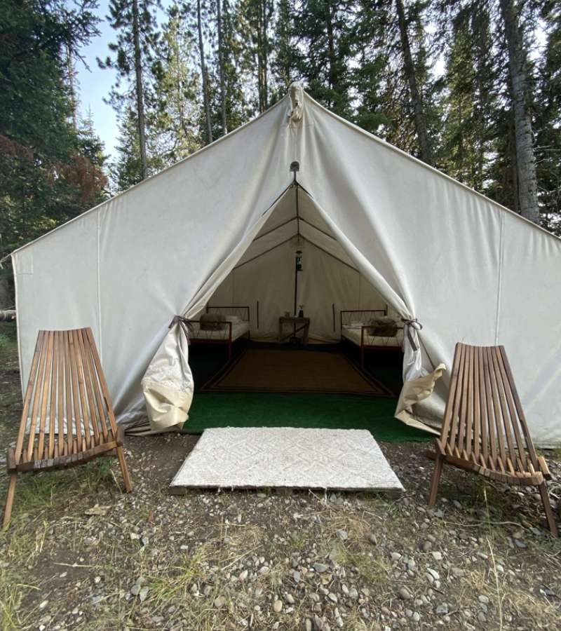 Two wooden chairs next to a canvas wall tent with the door flaps open.